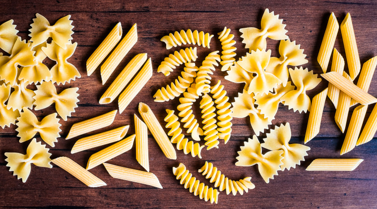 Variety of types and shapes of dry Italian pasta - fusilli, farfalle and penne, top view. Uncooked whole wheat italian pasta. Image with copy space.