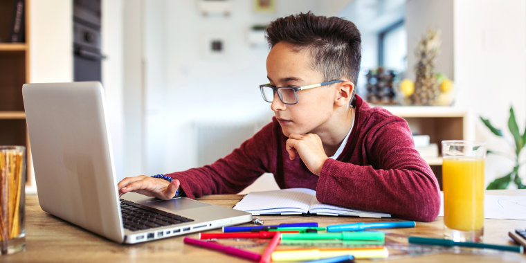 Boy doing homework on laptop surrounded by school supplies