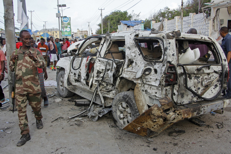 Image: A member of the security forces walks past a wrecked vehicle outside the Elite Hotel in Mogadishu, Somalia