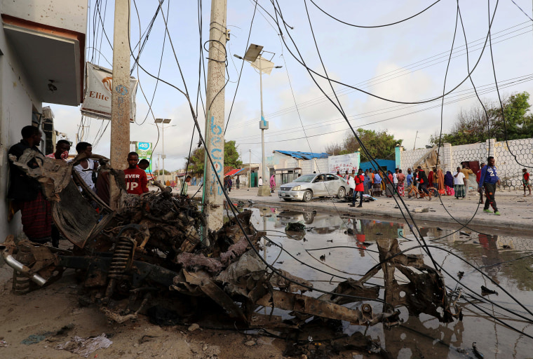 Image: Civilians near the wreckage of a car destroyed at the scene of a militant attack at the Elite Hotel in Lido beach, in Mogadishu, Somalia