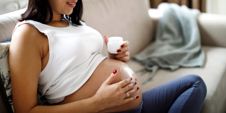 Pregnant woman sitting on couch applying stretch mark cream to stomach