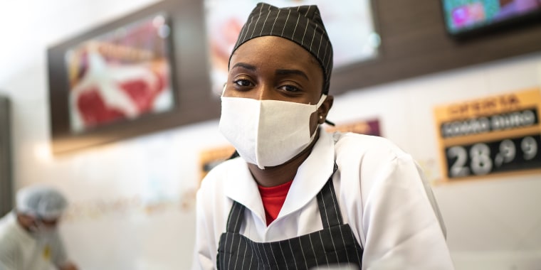 Portrait of female butcher working at butcher's shop - with face mask
