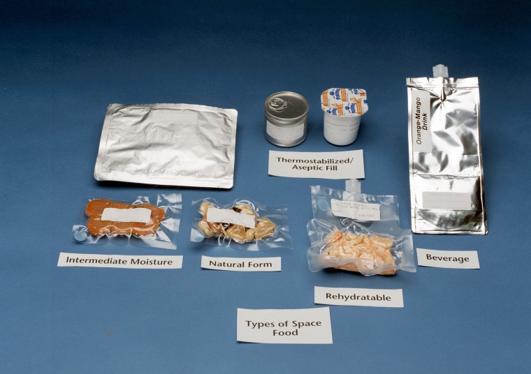 A space station meal tray with packaged food and drink, including rehydratable shrimp cocktail, rehydratable coffee and cream and irradiated steak.