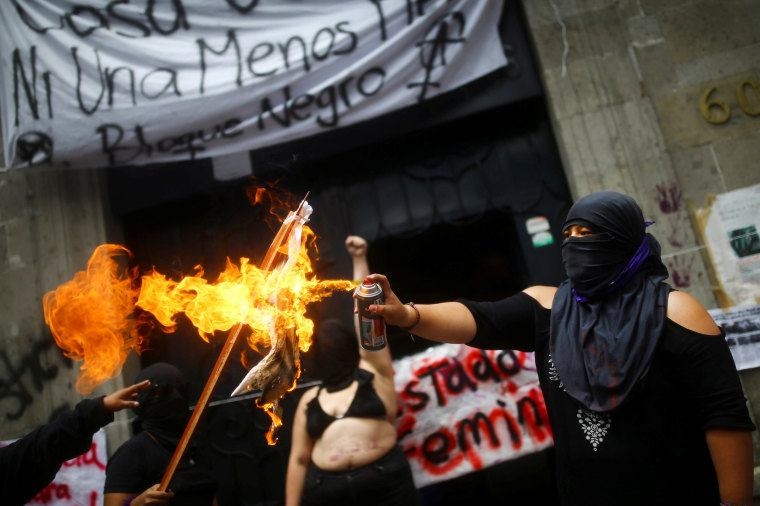 Image: A feminist activist burns a flag outside the National Human Rights Commission building after seizing the facilities of the organization for demand justice for the victims of gender violence and femicide in Mexico City
