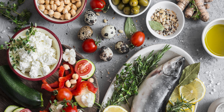 Mediterranean style food background. Fish, vegetables, herbs, chickpeas, olives, cheese on grey background, top view. Healthy food concept. Flat lay