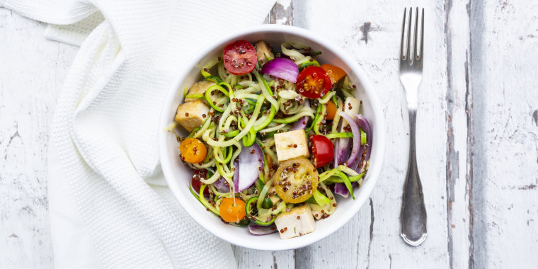 Bowl of zoodles with fried tofu, red quinoa, red onions and tomatoes
