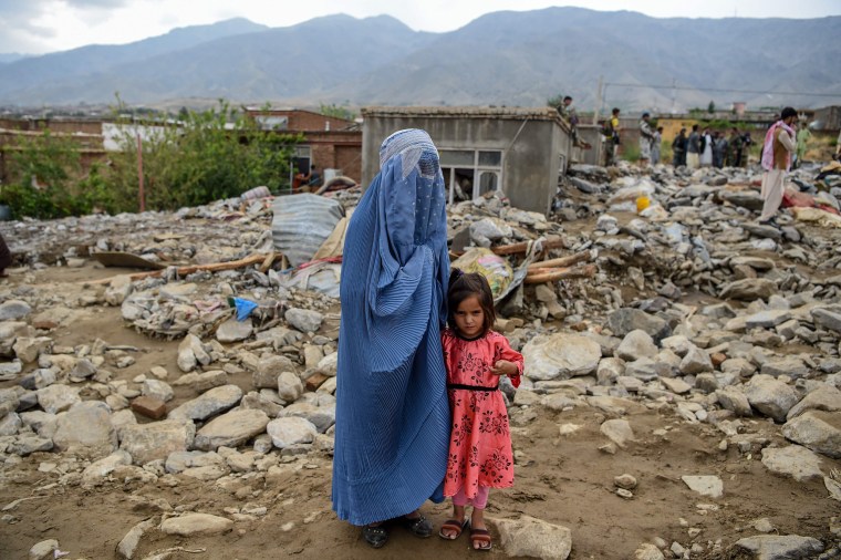 Image: A burqa-clad woman stands near a young girl among households' debris after a flash flood affected the area at Sayrah-e-Hopiyan in Charikar, Afghanistan