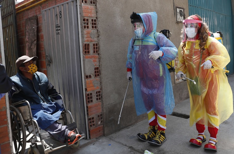 Image: Clowns Perlita and Tapetito, wearing protective gear amid the new coronavirus pandemic, speak with resident Enrique Zeballos as they arrive to disinfect his home free of charge, in El Alto, Bolivia