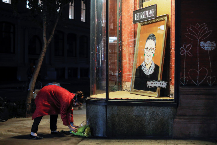 Image: A person places flowers in front of a painting in a storefront on Broadway of Associate Justice of the Supreme Court of the United States Ruth Bader Ginsburg who passed away in Manhattan, New York City