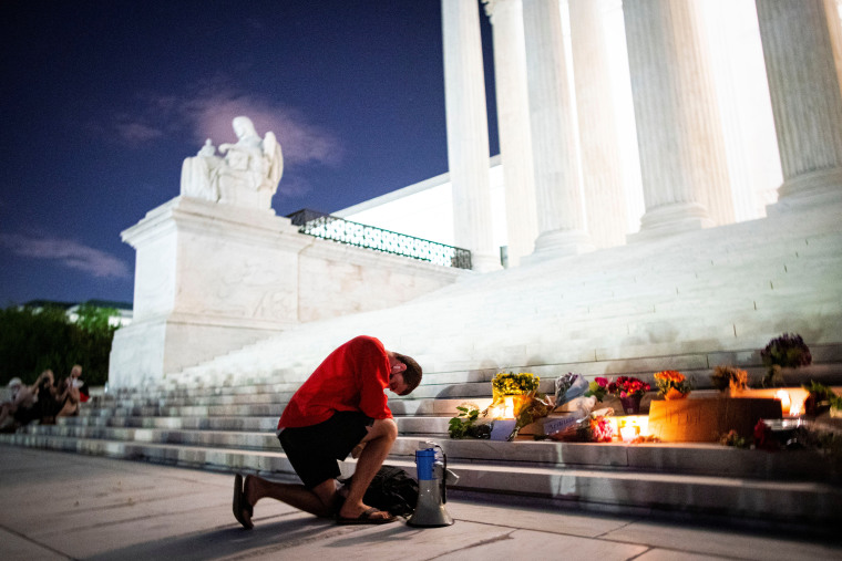 Image: A man kneels as he brings a megaphone to a vigil on the steps of the U.S. Supreme Court following the death of U.S. Supreme Court Justice Ruth Bader Ginsburg, in Washington