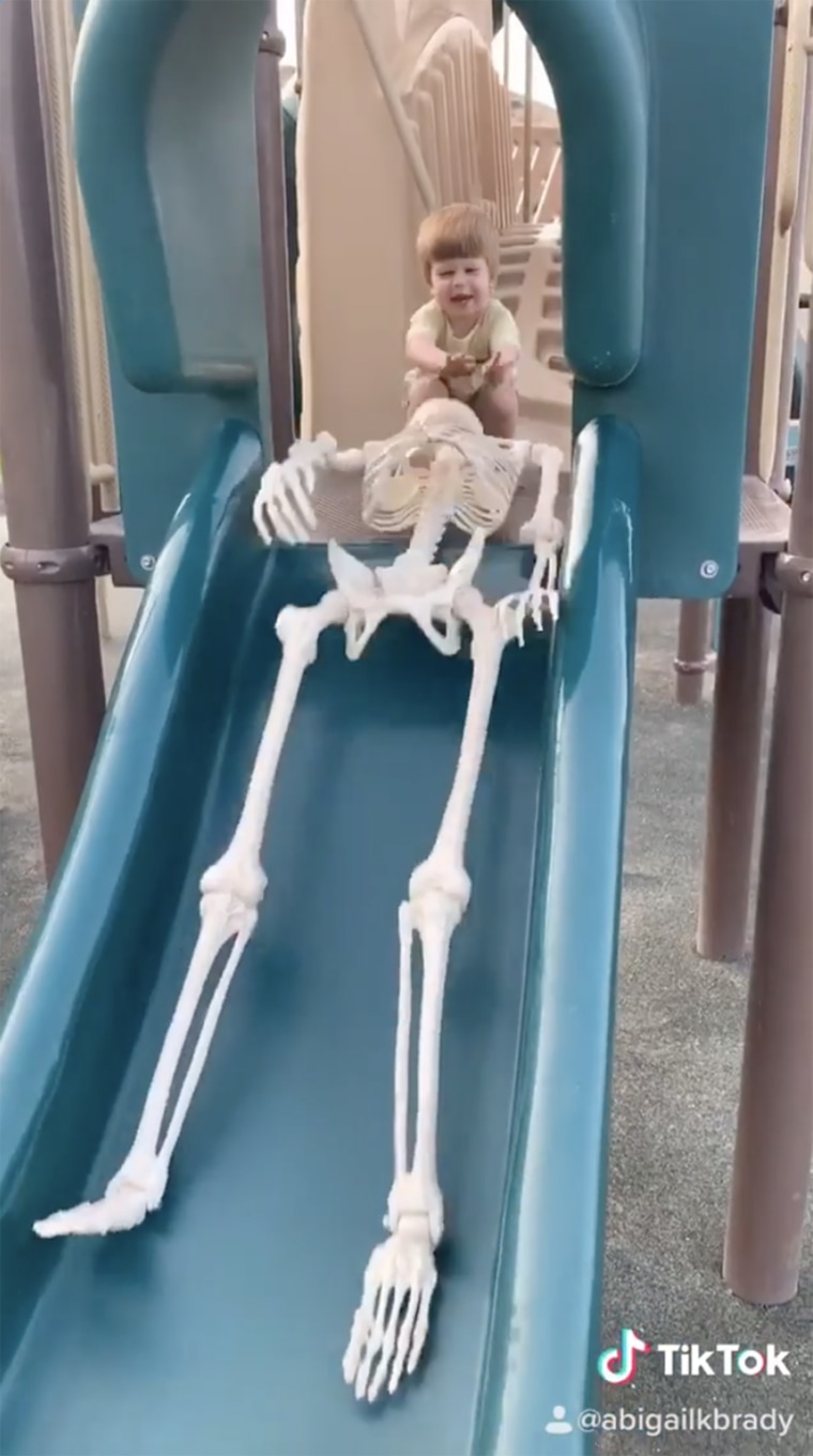 Toddler pushes skeleton down a slide.