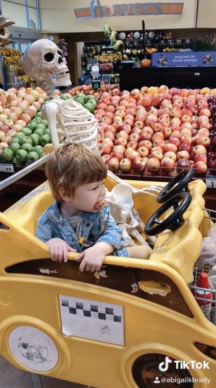 Theo and Benny the skeleton ride together in grocery cart.