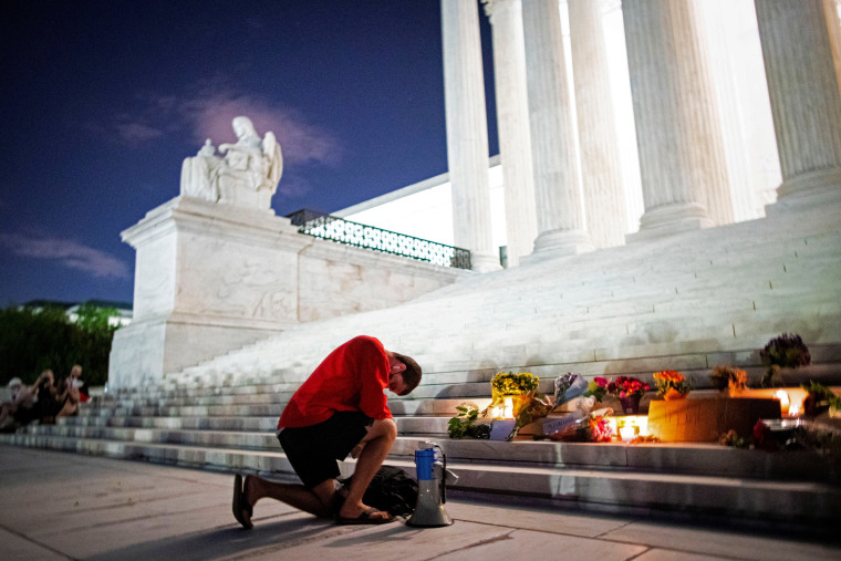 Image: A man kneels as he brings a megaphone to a vigil on the steps of the U.S. Supreme Court following the death of U.S. Supreme Court Justice Ruth Bader Ginsburg, in Washington