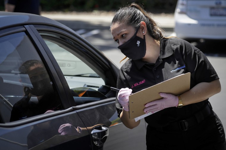 Jennifer Majano helps a job seeker fill out an application at a drive-up job fair for Allied Universal on May 6, 2020, in Gardena, Calif.