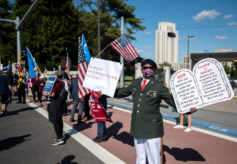 Image: Lewis Bracy holds protest signs while standing near supporters of President Donald Trump near Walter Reed National Military Medical Center on Oct. 3, 2020.