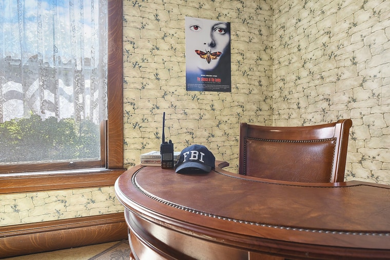 A poster for the movie hangs on one wall of the home with some FBI props featured on a desk. 