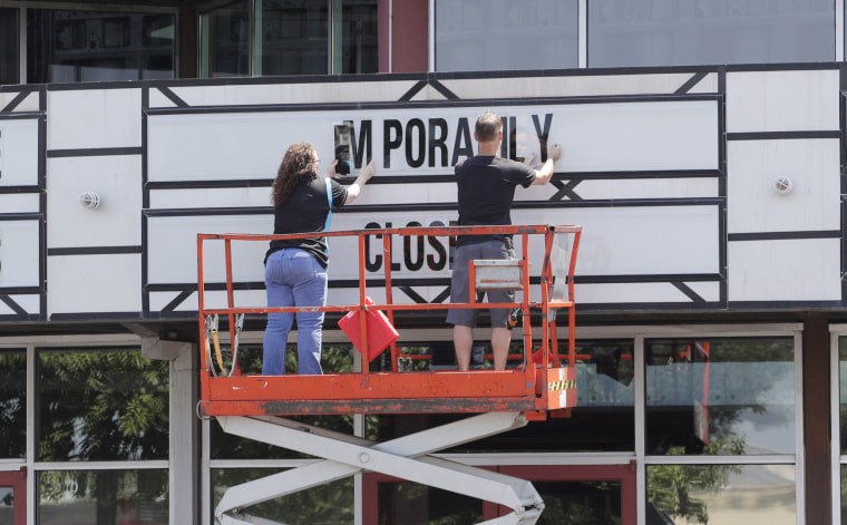 Workers remove a sign saying "Temporarily Closed" on the marquee at the Quarry Cinema in San Antonio on May 4.