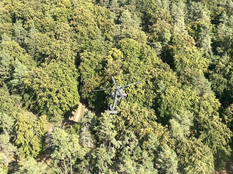 Image: A Boeing AH-64 Apache helicopter hovering over woodland during a ten-day, multi-national military exercise at the U.S. Army's Hohenfels training area