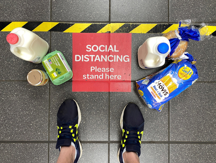 Image: Food shopping next to a social distancing sign at a British supermarket in April.