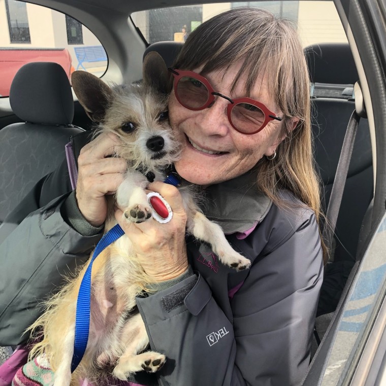 A woman in a car snuggles a dog.