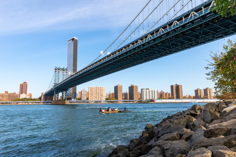 The raft sails under a bridge spanning the East River. 