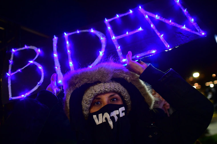 Image: Christie Tan holds an illuminated BIDEN sign at a drive-in election eve rally in Philadelphia