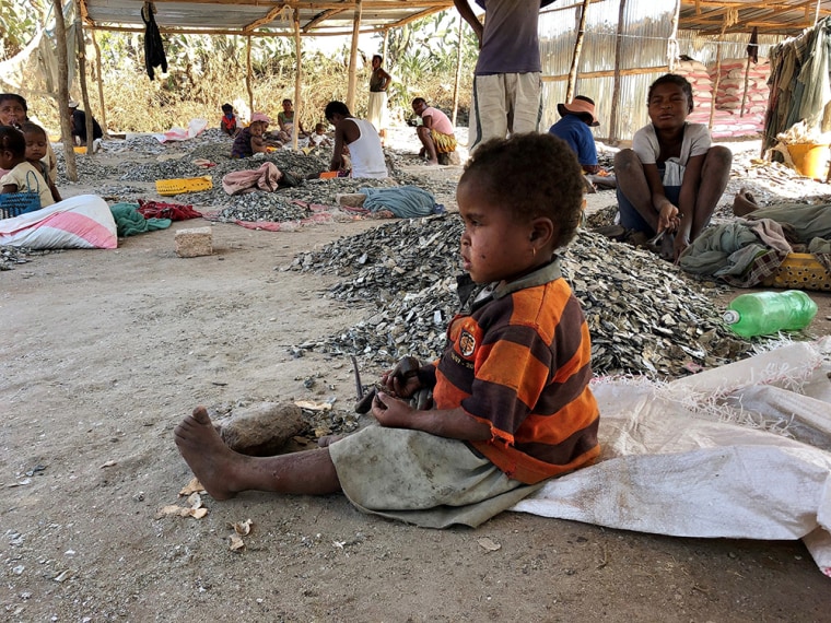 A three-year-old girl, works alongside her mother, breaking down blocks of mica.