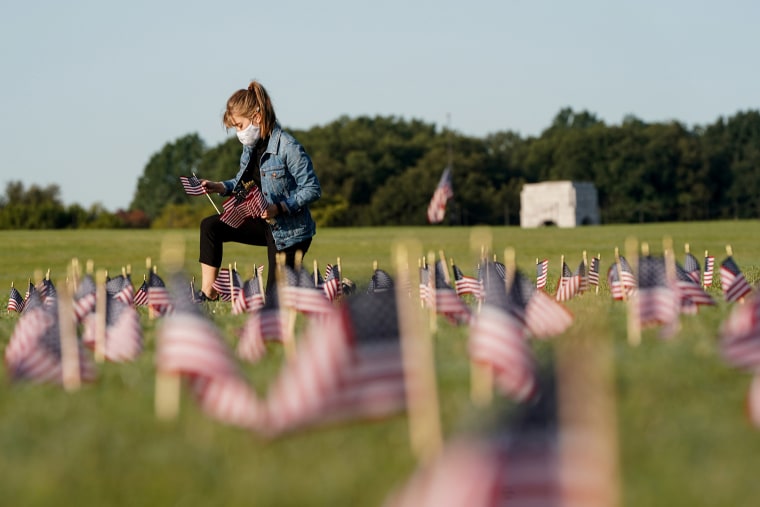 Image: A volunteer places American flags representing some of the 200,000 lives lost in the United States in the coronavirus disease (COVID-19) pandemic on the National Mall in Washington