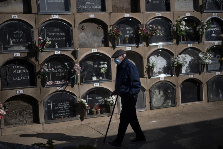 Image: A man wearing face mask walks next to graves decorated with flowers in tribute of deceased relatives at the cemetery during All Saints Day in Barcelona, Spain.