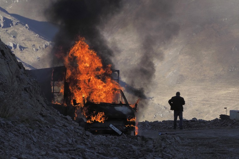 Image: A man stands near his burning car which caught on fire during the climb along the road to a mountain pass, near the border between Nagorno-Karabakh and Armenia
