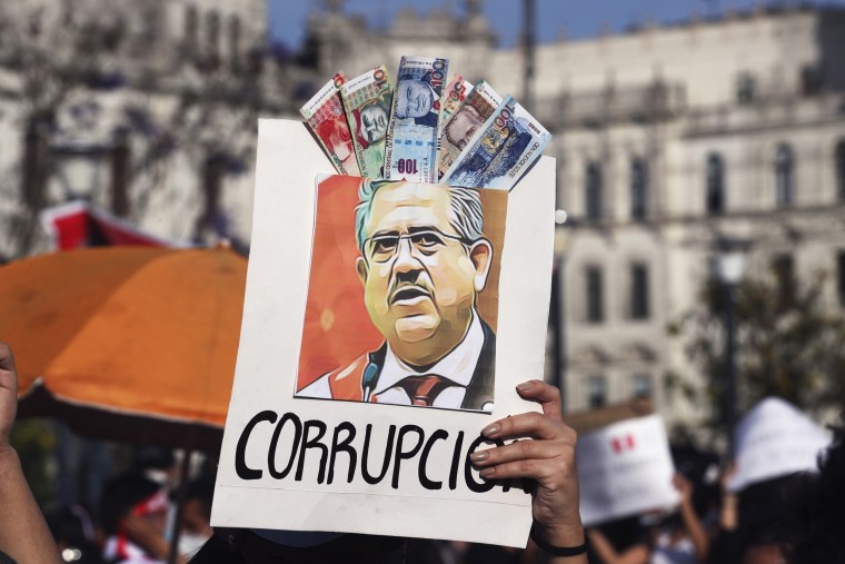 A protester holds up a poster adorned with play money and the Spanish word for corruption around a depiction Peru's newly sworn-in president Manuel Merino in Lima on Nov. 14, 2020.