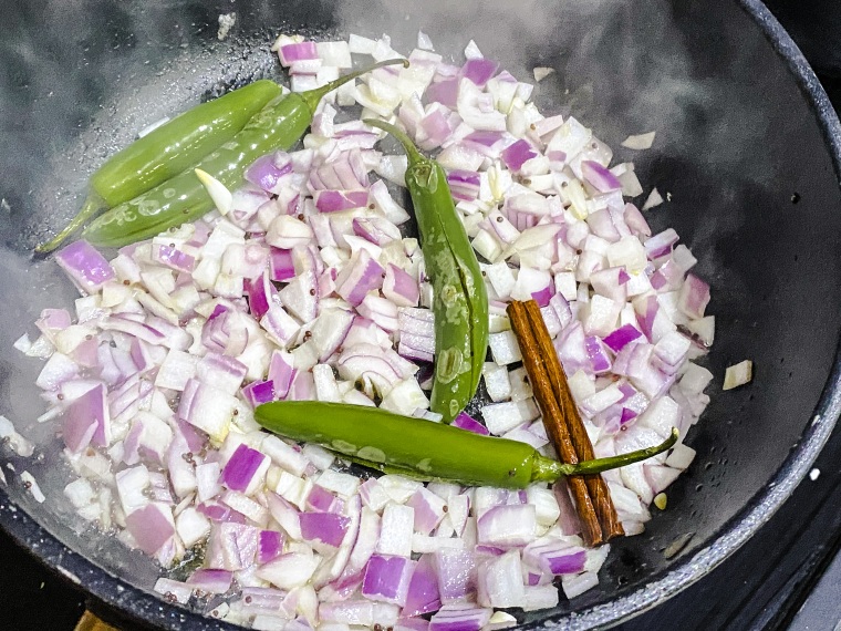 Before adding the marinated chicken thighs to the pan, the recipe calls for cooking fresh green chiles with red onion and cinnamon.