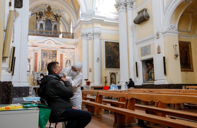 Image: A member of the medical personnel wearing protective clothing takes a swab from a man in the coronavirus disease (COVID-19) testing centre at San Severo fuori le mura church, in Naples, Italy