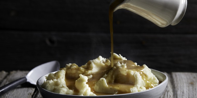Jug of gravy being poured onto bowl of steaming mashed potatoes, studio shot