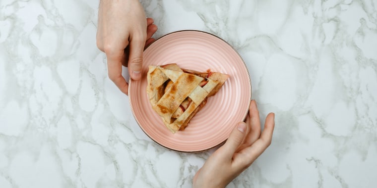 Flatlay of men passing the piece of apple pie to woman's hand on marble background