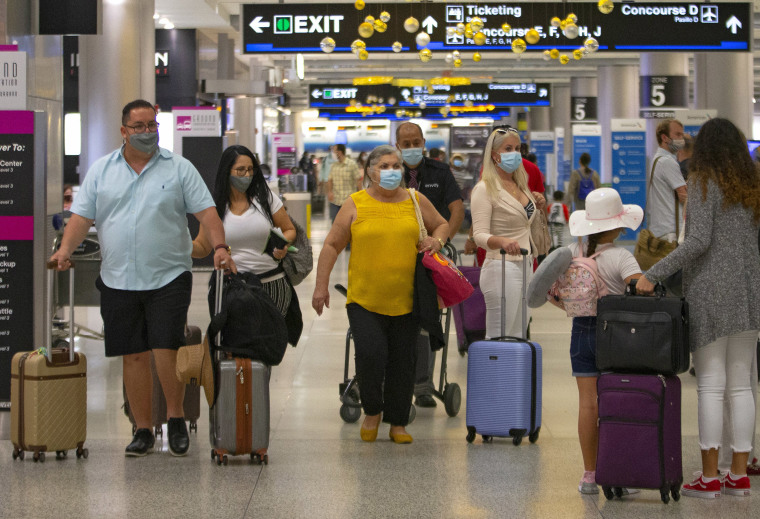 Image: Travelers wearing protective face masks walking through Concourse D at the Miami International Airport