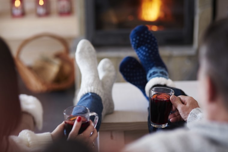 A couple with hot drinks in living room at the fireplace.