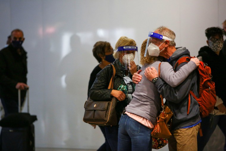 Image: Travelers wearing protective face masks and face shields to prevent the spread of Covid-19 hug at the airport in Denver, on Tuesday.