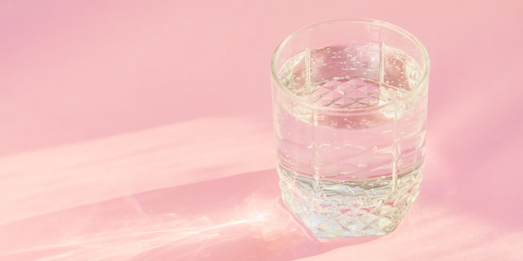 Close up of sparkling water in transparent glass and sun glare on pink background.