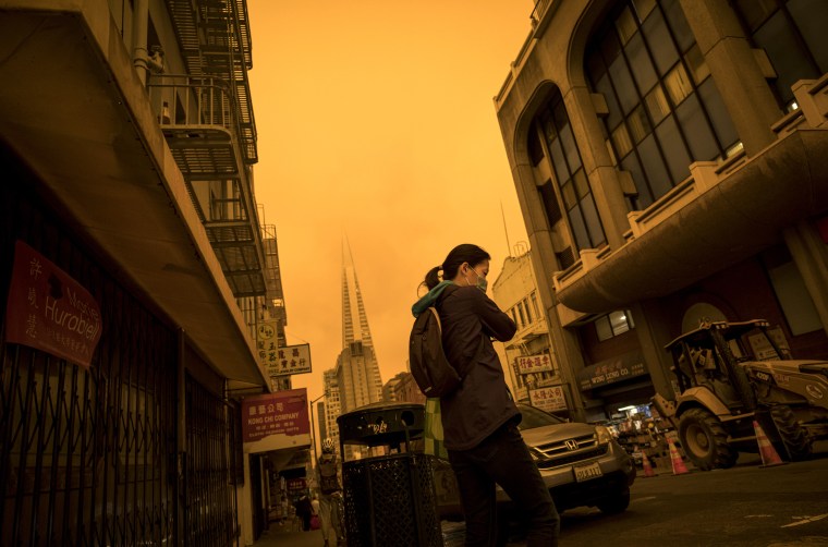 Image: A person wearing a mask walks in San Francisco's Chinatown as smoke from nearby wildfires clog the sky on Sept. 9, 2020.