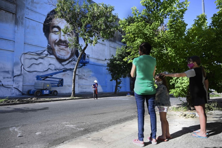 Image: People watch Argentine street artist Alfredo Segatori painting a mural of late Argentine football legend Diego Maradona in Buenos Aires