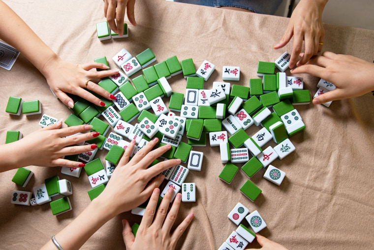 People mixing tiles while playing Chinese board game Mahjong at home