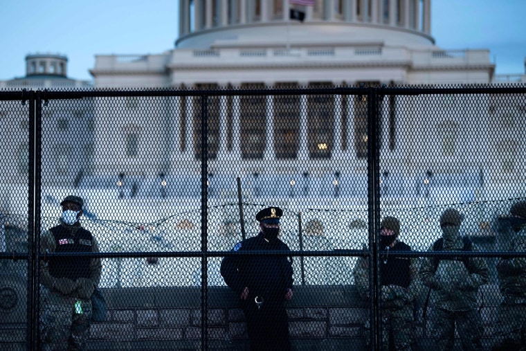 Image: A Capitol Police officer stands with members of the National Guard behind a crowd control fence surrounding Capitol Hill