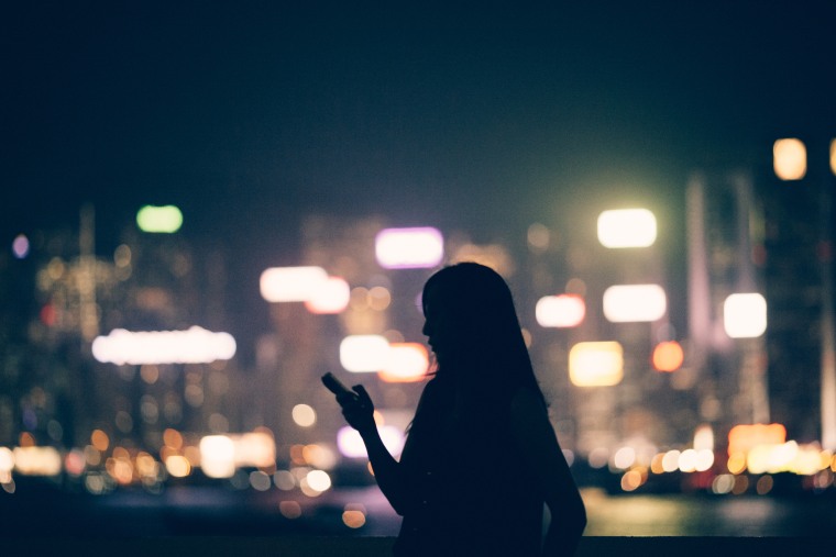 Silhouette of woman using a smartphone in a city at night.