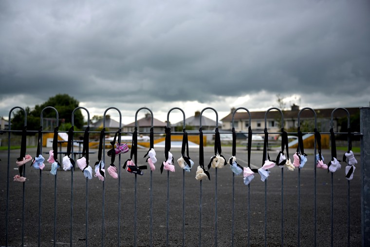 Image: Infant and baby shoes are hung along the playground fence as a vigil is held at the Tuam Mother and Baby home mass burial site