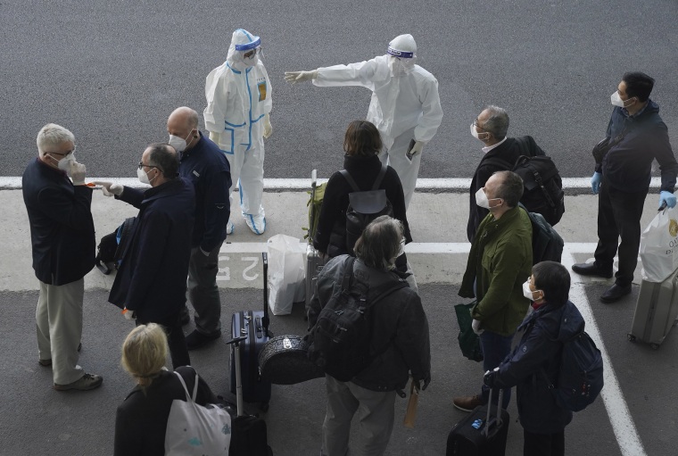 Image: A worker in protective coverings directs members of the World Health Organization (WHO) team on their arrival at the airport in Wuhan