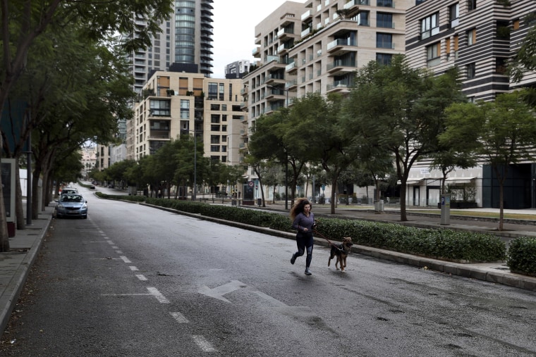 Image: A woman runs with her dog in an almost empty street in Beirut on Thursday as Lebanese authorities began enforcing an 11-day nationwide shutdown and round the clock curfew.