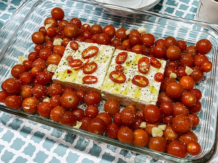 To make the dish, start by adding some olive oil to the bottom of a pan then place a block of feta in the center and surround it with tomatoes.