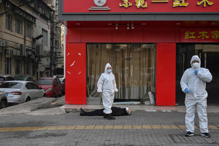 Image: Officials in protective suits checking on an elderly man wearing a facemask who collapsed and died on a street near a hospital in Wuhan