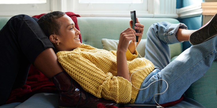 Woman relaxing on her couch with her partner while listening to music and playing on her phone